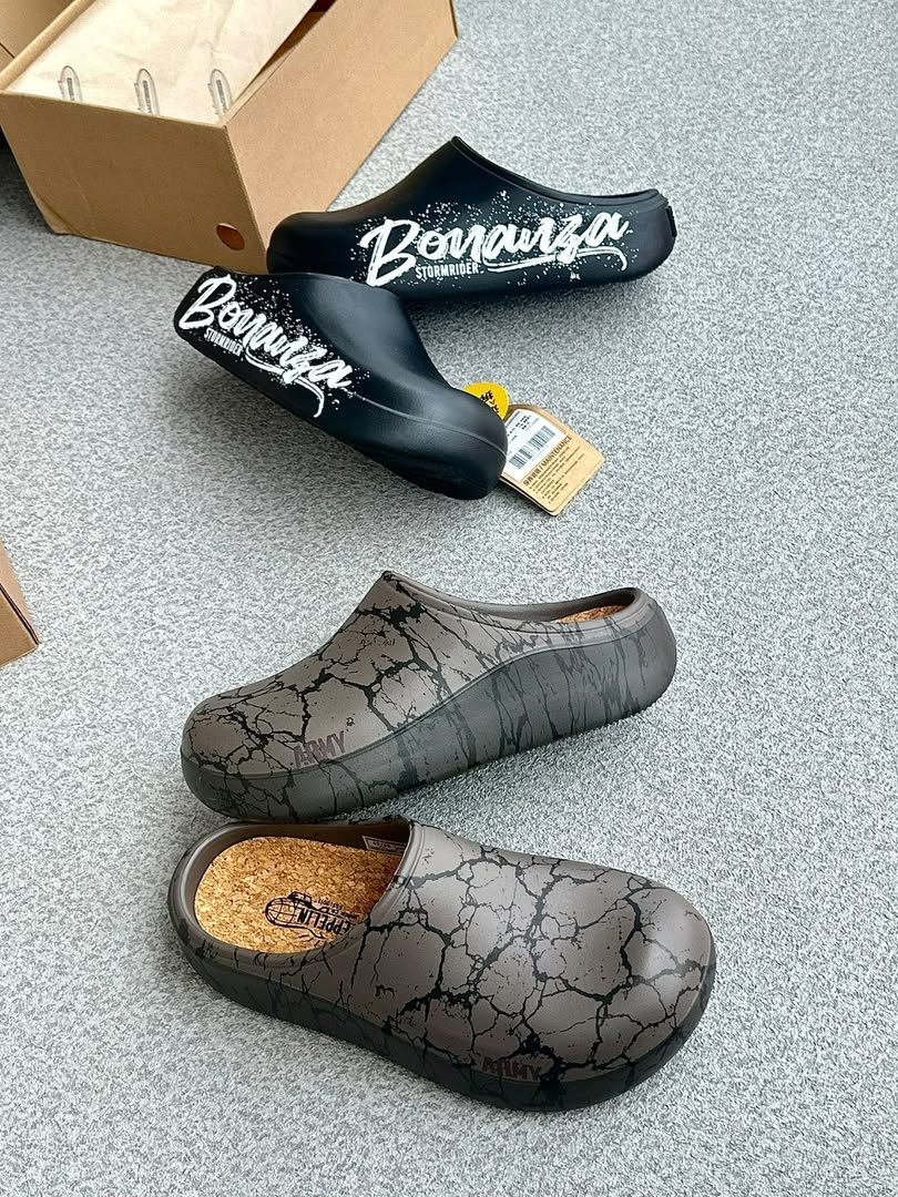 root A pair of black clogs with white Bonanza Storm Rider branding and a pair of grey clogs with a cracked pattern, showcasing modern luxury footwear.