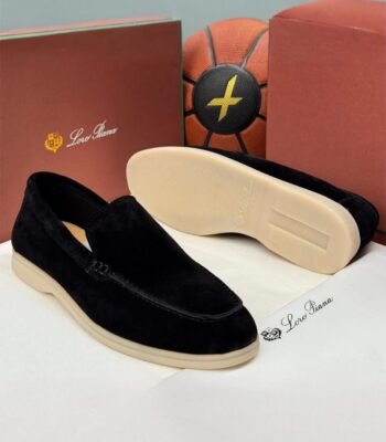 A pair of black velvet loafers with beige soles, displayed on a white surface with Loro Piana branding and packaging in the background.