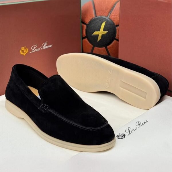 A pair of black velvet loafers with beige soles, displayed on a white surface with Loro Piana branding and packaging in the background.