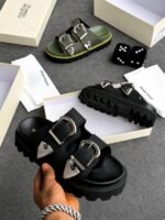 A pair of black sandals with silver buckles, showcased in a luxurious setting with Alexander McQueen branding, exuding Modern Luxury and Urban Edge.