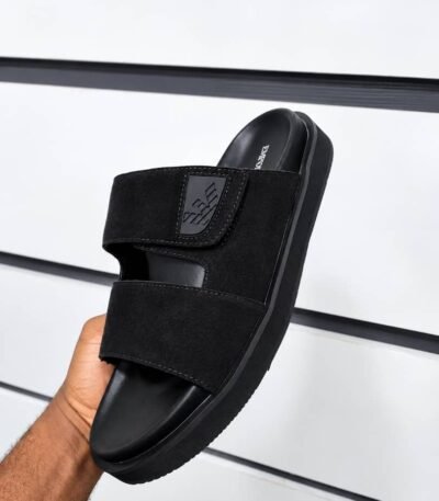 A hand holding a black slide with two wide straps and a thick sole, showcasing Modern Luxury and Urban Edge design.
