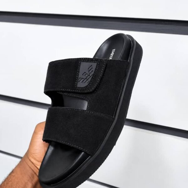A hand holding a black slide with two wide straps and a thick sole, showcasing Modern Luxury and Urban Edge design.