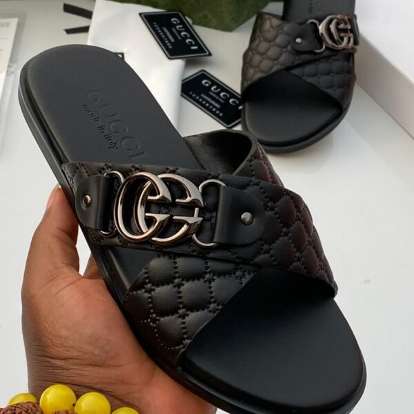 A pair of luxurious black Gucci slides with gold-tone buckle and quilted design, presented on a white surface with Gucci packaging in the background.