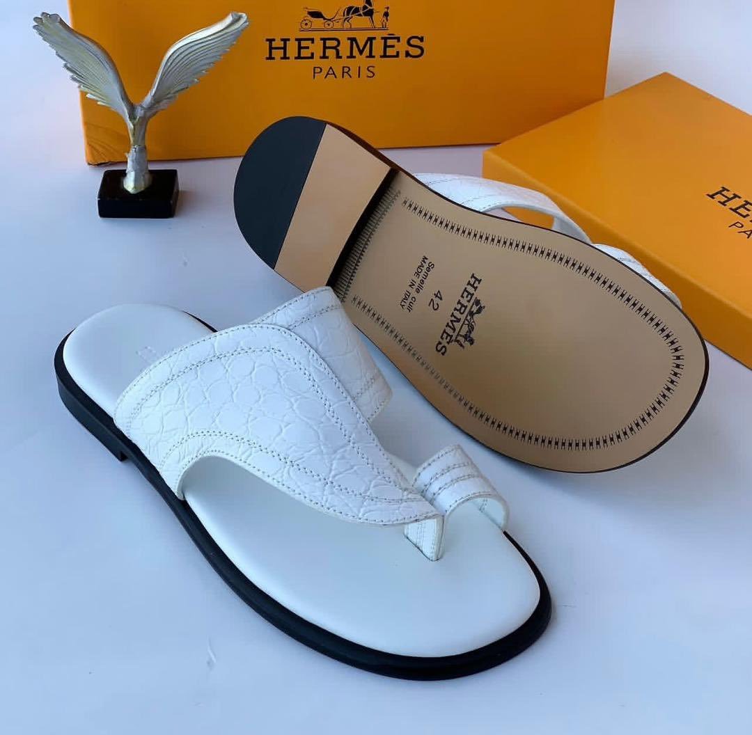 root A pair of white leather slides with black soles, displayed with Hermes Paris branding and packaging, embodying Modern Luxury and Urban Edge.