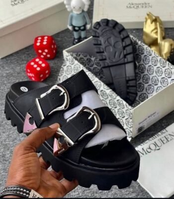 A pair of black sandals with silver buckles, showcased in a luxurious setting with Alexander McQueen branding, exuding Modern Luxury and Urban Edge.