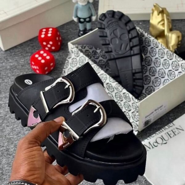 A pair of black sandals with silver buckles, showcased in a luxurious setting with Alexander McQueen branding, exuding Modern Luxury and Urban Edge.