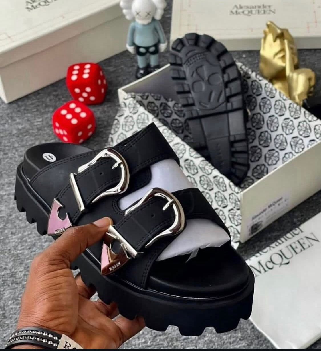 root A pair of black sandals with silver buckles, showcased in a luxurious setting with Alexander McQueen branding, exuding Modern Luxury and Urban Edge.
