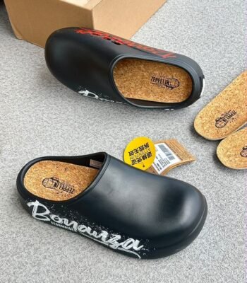 A pair of black clogs with cork insoles and graffiti-inspired design on a grey surface.