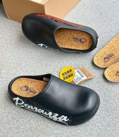 A pair of black clogs with cork insoles and graffiti-inspired design on a grey surface.