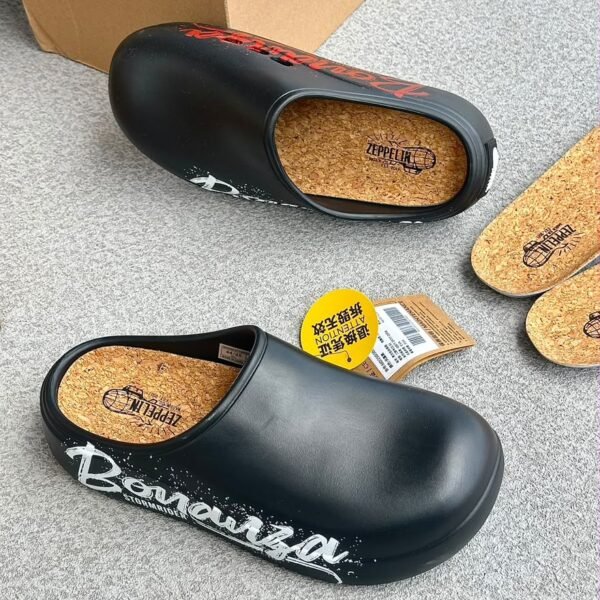 A pair of black clogs with cork insoles and graffiti-inspired design on a grey surface.