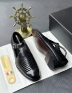 A pair of luxurious black leather monk strap shoes on a white cloth, accompanied by a shoe tree and a decorative ship's wheel, exuding modern luxury and urban edge.