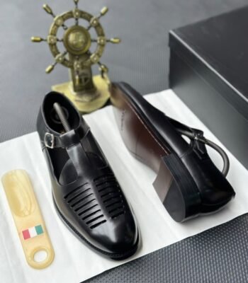 A pair of luxurious black leather monk strap shoes on a white cloth, accompanied by a shoe tree and a decorative ship's wheel, exuding modern luxury and urban edge.