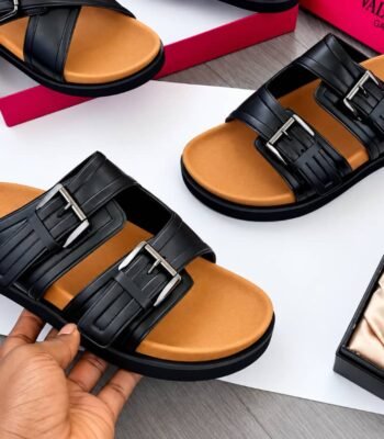 A pair of luxurious black sandals with double-strap design and silver buckles, showcased on a white background with a red shoe box and a bottle of perfume.