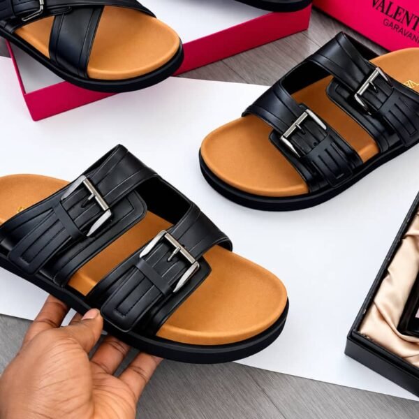 A pair of luxurious black sandals with double-strap design and silver buckles, showcased on a white background with a red shoe box and a bottle of perfume.