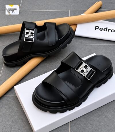 A pair of black leather sandals with silver buckles, placed on a white shoe box and a grey tiled floor, exuding Modern Luxury and Urban Edge.