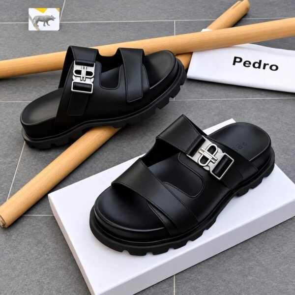 A pair of black leather sandals with silver buckles, placed on a white shoe box and a grey tiled floor, exuding Modern Luxury and Urban Edge.