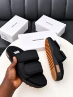 A pair of black slides with orange soles, presented on a white table with white boxes in the background, embodying Modern Luxury and Urban Edge.
