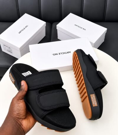 A pair of black slides with orange soles, presented on a white table with white boxes in the background, embodying Modern Luxury and Urban Edge.