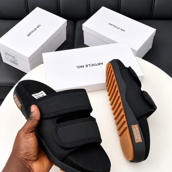A pair of black slides with orange soles, presented on a white table with white boxes in the background, embodying Modern Luxury and Urban Edge.