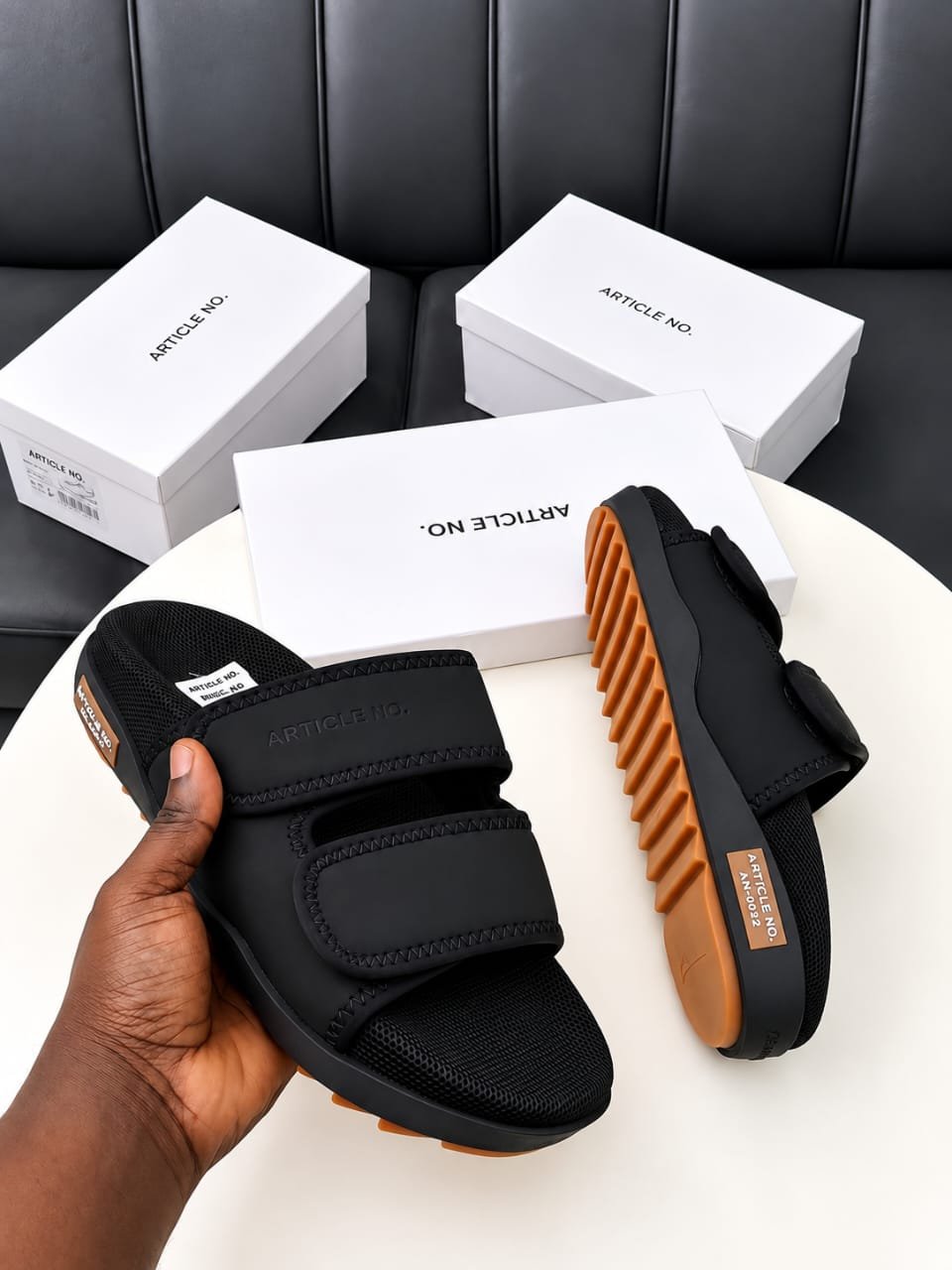 root A pair of black slides with orange soles, presented on a white table with white boxes in the background, embodying Modern Luxury and Urban Edge.