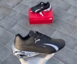 A pair of black and white Puma sneakers, one placed on a red shoe box and the other held by a hand, showcasing the shoe's sleek design and luxurious appeal.