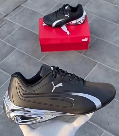 A pair of black and white Puma sneakers, one placed on a red shoe box and the other held by a hand, showcasing the shoe's sleek design and luxurious appeal.