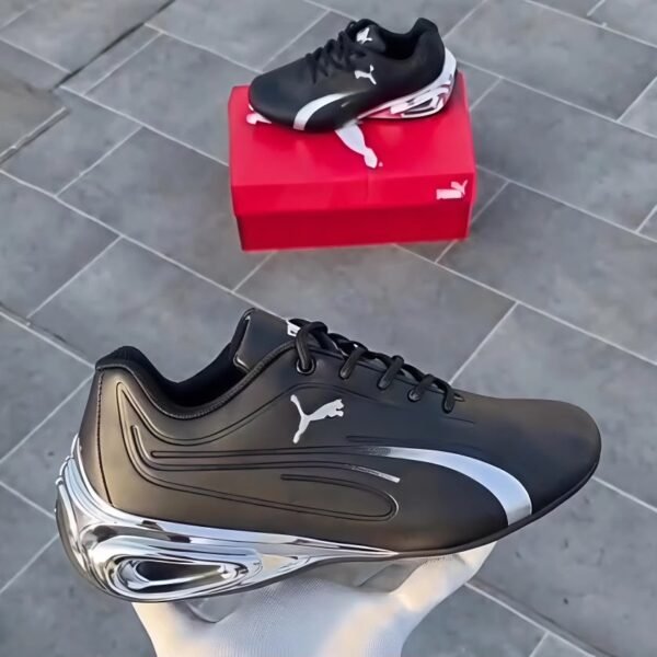 A pair of black and white Puma sneakers, one placed on a red shoe box and the other held by a hand, showcasing the shoe's sleek design and luxurious appeal.