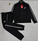 A luxurious black tracksuit with grey stripes and Nike logo, laid out on a grey surface.