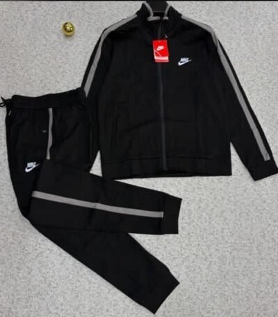 A luxurious black tracksuit with grey stripes and Nike logo, laid out on a grey surface.