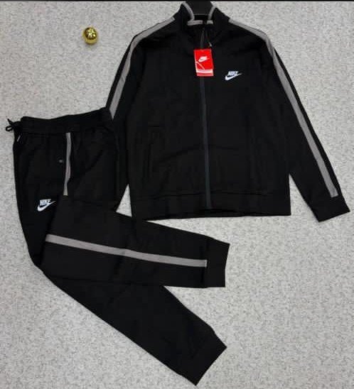 A luxurious black tracksuit with grey stripes and Nike logo, laid out on a grey surface.