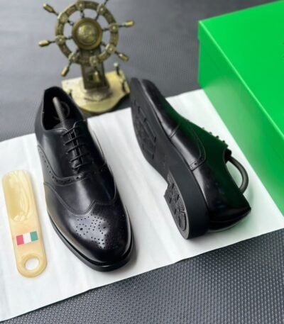 A pair of black leather oxfords with brogue detailing, accompanied by a shoe tree and presented on a crisp white background, evoking a sense of luxury and refinement.