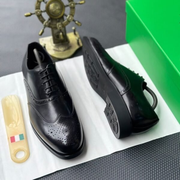 A pair of black leather oxfords with brogue detailing, accompanied by a shoe tree and presented on a crisp white background, evoking a sense of luxury and refinement.