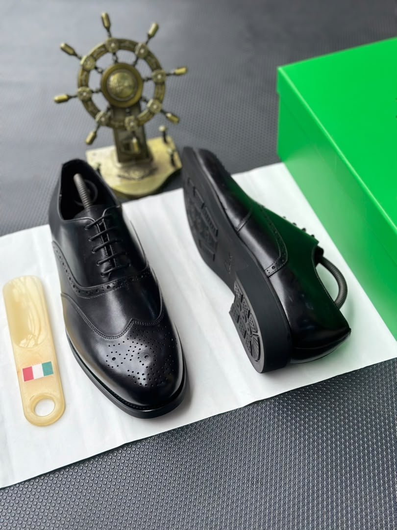 root A pair of black leather oxfords with brogue detailing, accompanied by a shoe tree and presented on a crisp white background, evoking a sense of luxury and refinement.