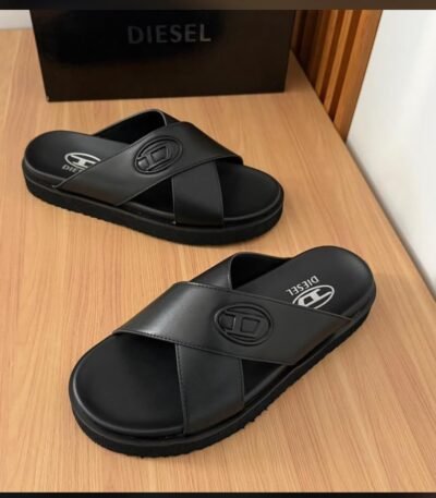 A pair of black Diesel slides with white logo on a wooden table next to a black box.