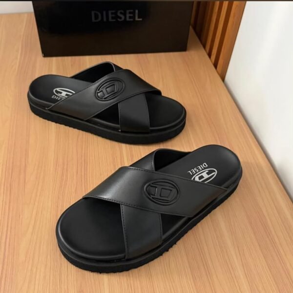A pair of black Diesel slides with white logo on a wooden table next to a black box.