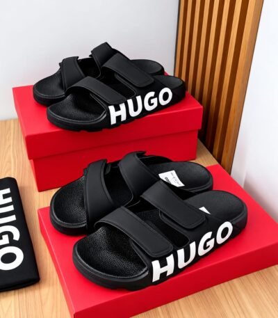 A pair of black HUGO slides on a red shoe box, exuding Modern Luxury and Urban Edge.