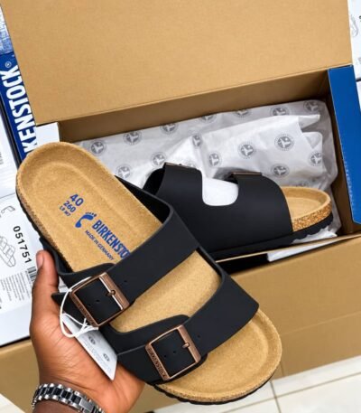 Birkenstock Arizona Slide in black, featuring a contoured cork footbed and two adjustable buckle straps, presented in its packaging.