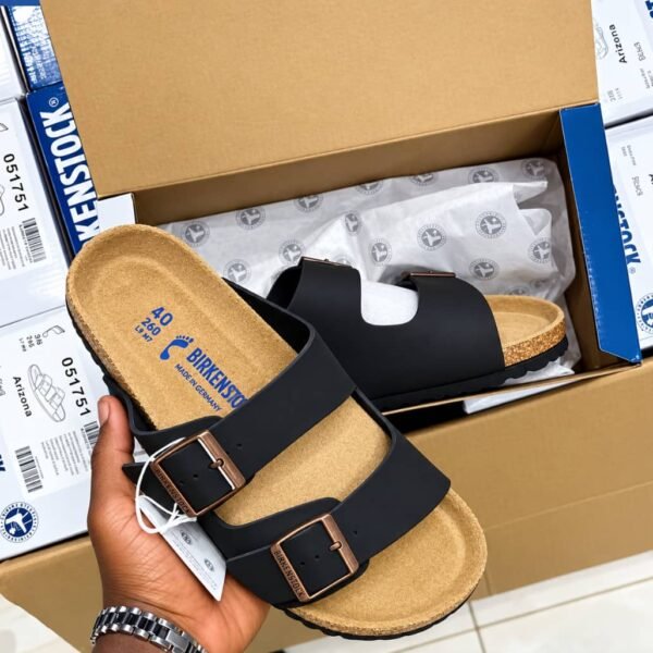 Birkenstock Arizona Slide in black, featuring a contoured cork footbed and two adjustable buckle straps, presented in its packaging.