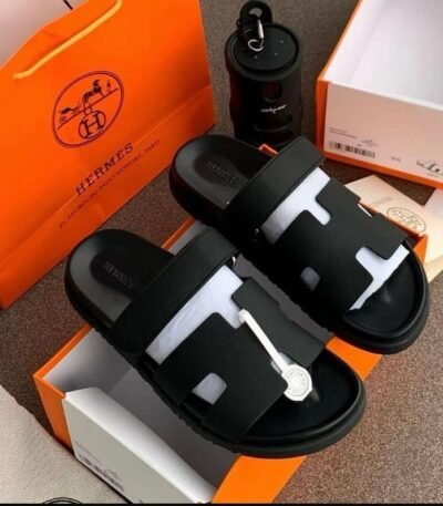 A pair of luxurious black slides nestled in an orange Hermes box, exuding Modern Luxury and Urban Edge.