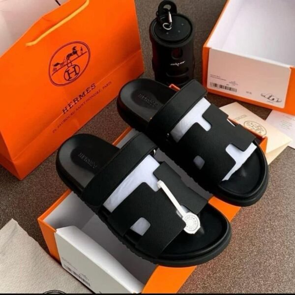A pair of luxurious black slides nestled in an orange Hermes box, exuding Modern Luxury and Urban Edge.