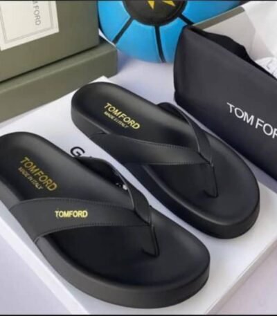 A pair of luxurious black Tom Ford flip-flops with gold lettering, presented on a white box with a black pouch and green box in the background.