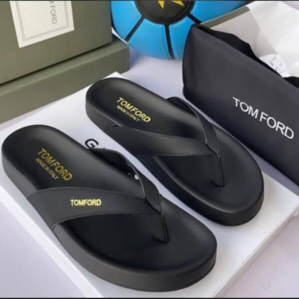 A pair of luxurious black Tom Ford flip-flops with gold lettering, presented on a white box with a black pouch and green box in the background.
