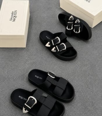 A pair of black slides with silver buckles and two white shoe boxes with 'Alexander McQueen' printed on them.