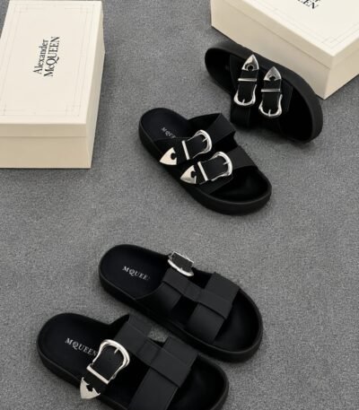 A pair of black slides with silver buckles and two white shoe boxes with 'Alexander McQueen' printed on them.