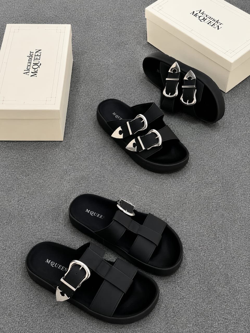 root A pair of black slides with silver buckles and two white shoe boxes with 'Alexander McQueen' printed on them.