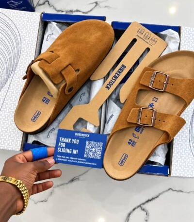 A pair of luxurious brown Birkenstock sandals, complete with suede straps and a cushioned footbed, nestled in a blue box on a marble surface.