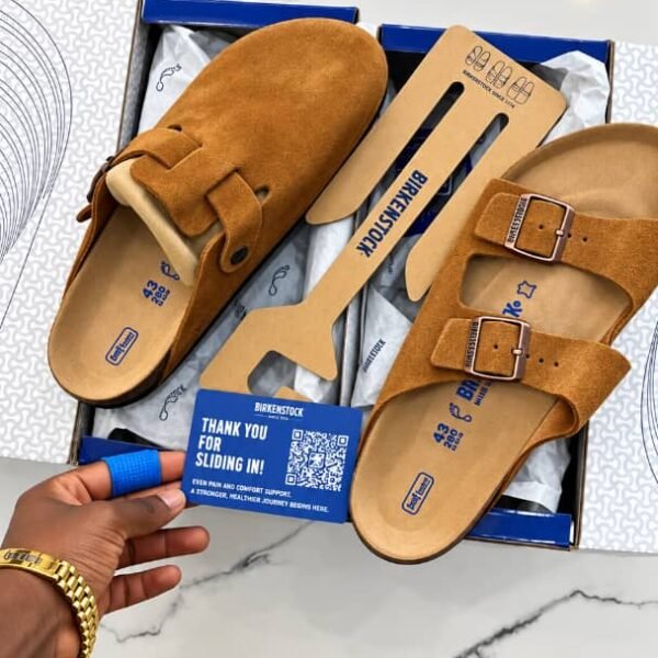 A pair of luxurious brown Birkenstock sandals, complete with suede straps and a cushioned footbed, nestled in a blue box on a marble surface.
