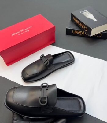 A pair of black leather half shoes with a buckle detail, accompanied by a red shoe box and luxury books.