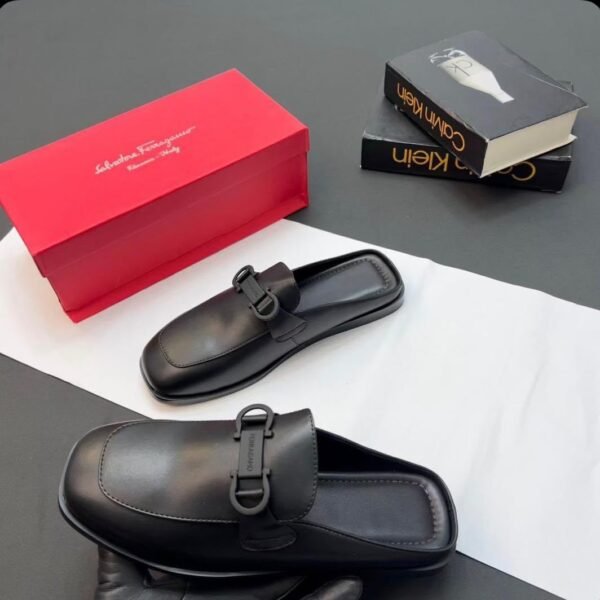A pair of black leather half shoes with a buckle detail, accompanied by a red shoe box and luxury books.