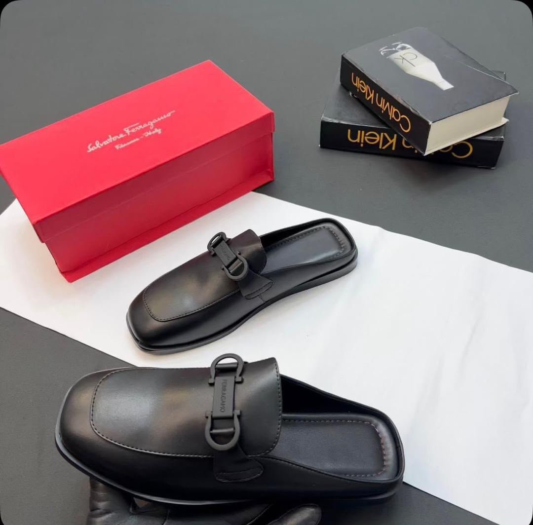 root A pair of black leather half shoes with a buckle detail, accompanied by a red shoe box and luxury books.